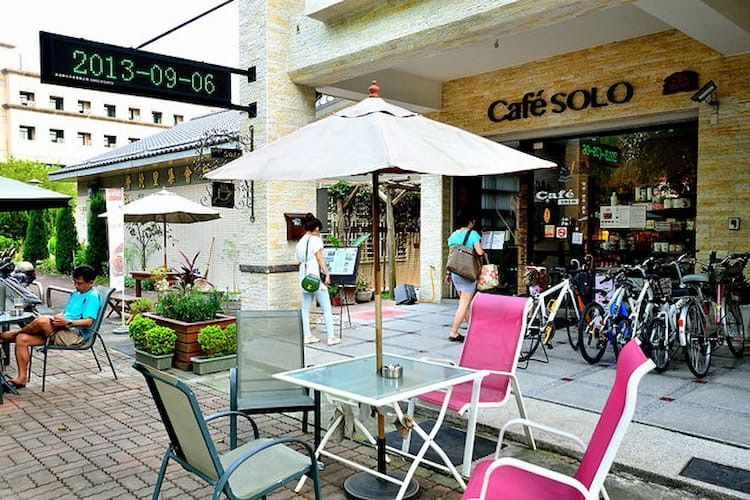 戶外咖啡館，配有白色遮陽傘、粉紅色椅子、自行車，以及「Cafe solo」店面。
