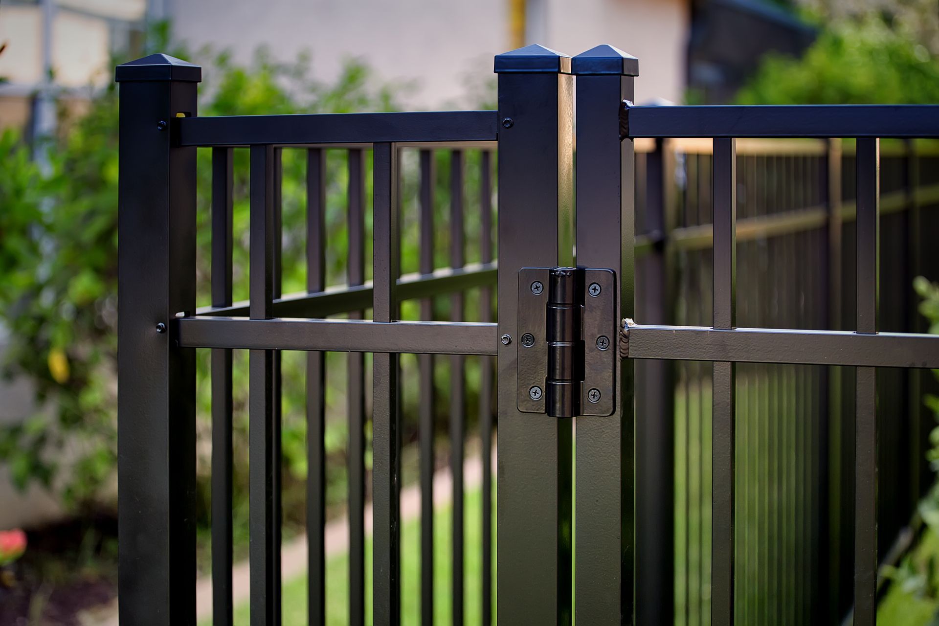 Black metal fence and gate with hinges and vertical bars, outdoors.