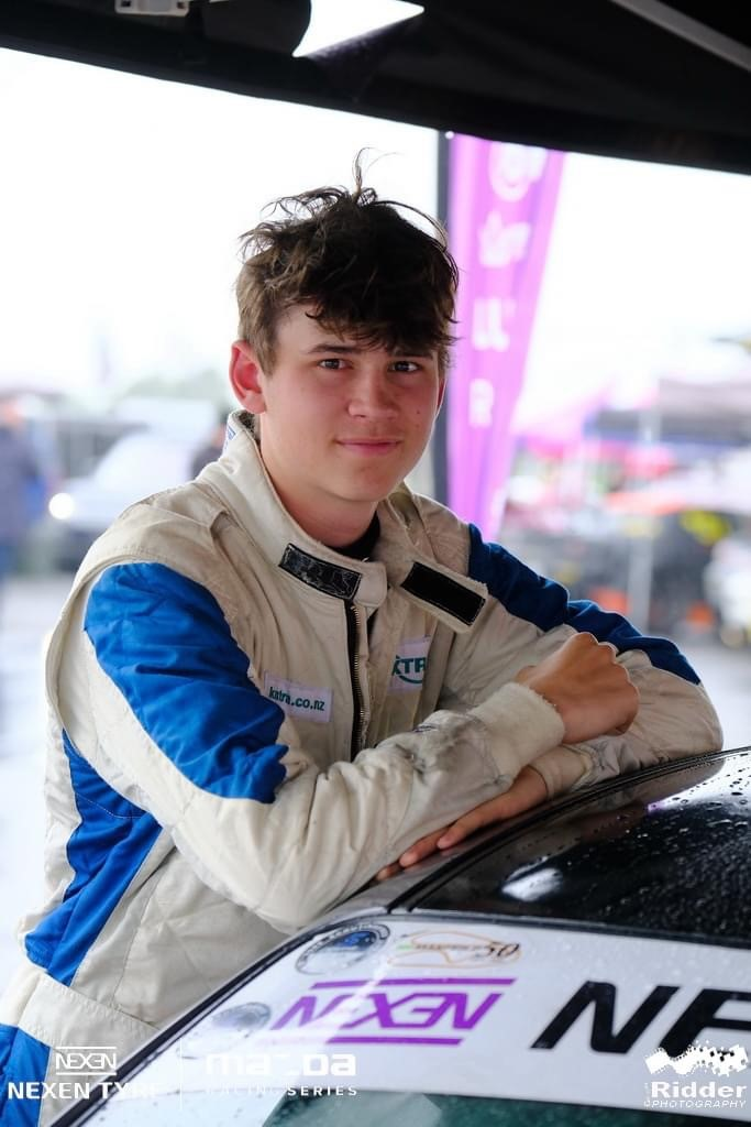 A young man is leaning on the hood of a race car.