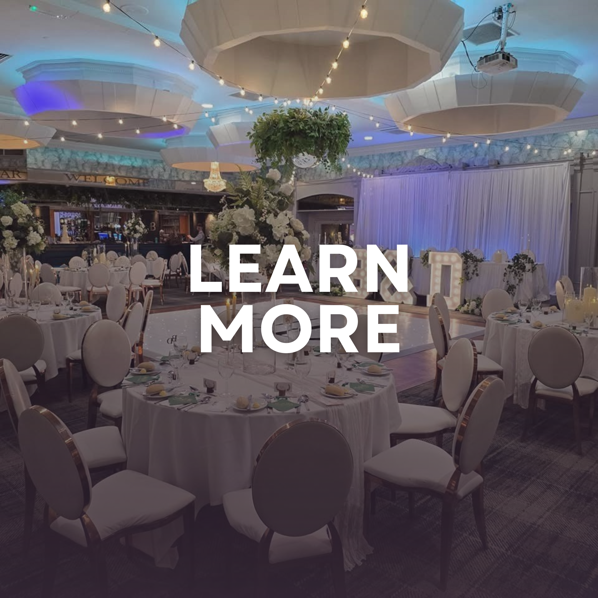 Elegant banquet hall with round white-clothed tables and blue lighting, overlaid with “LEARN MORE” text