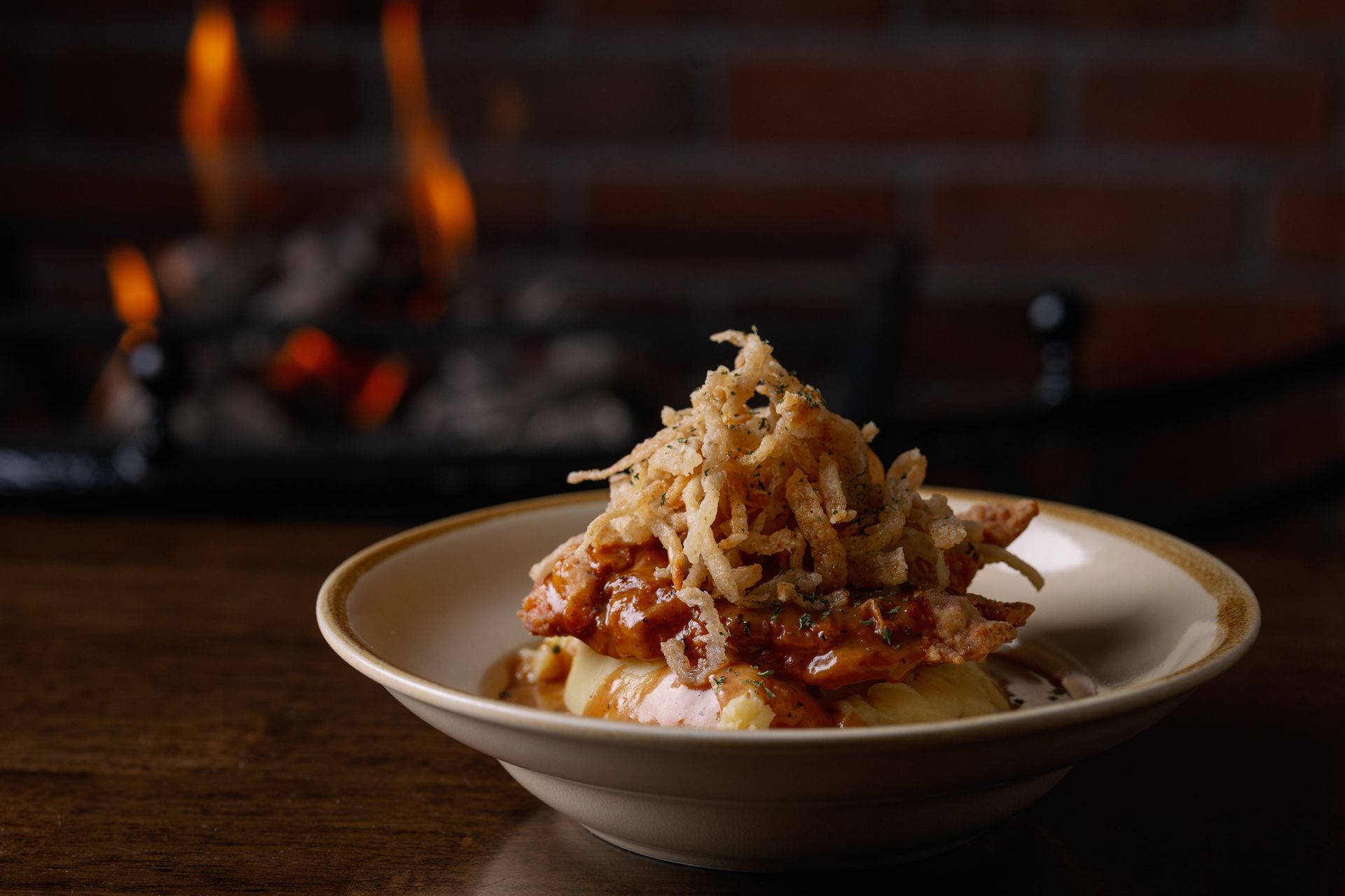 Pasta topped with grated cheese on a white plate, set in front of a lit fireplace.