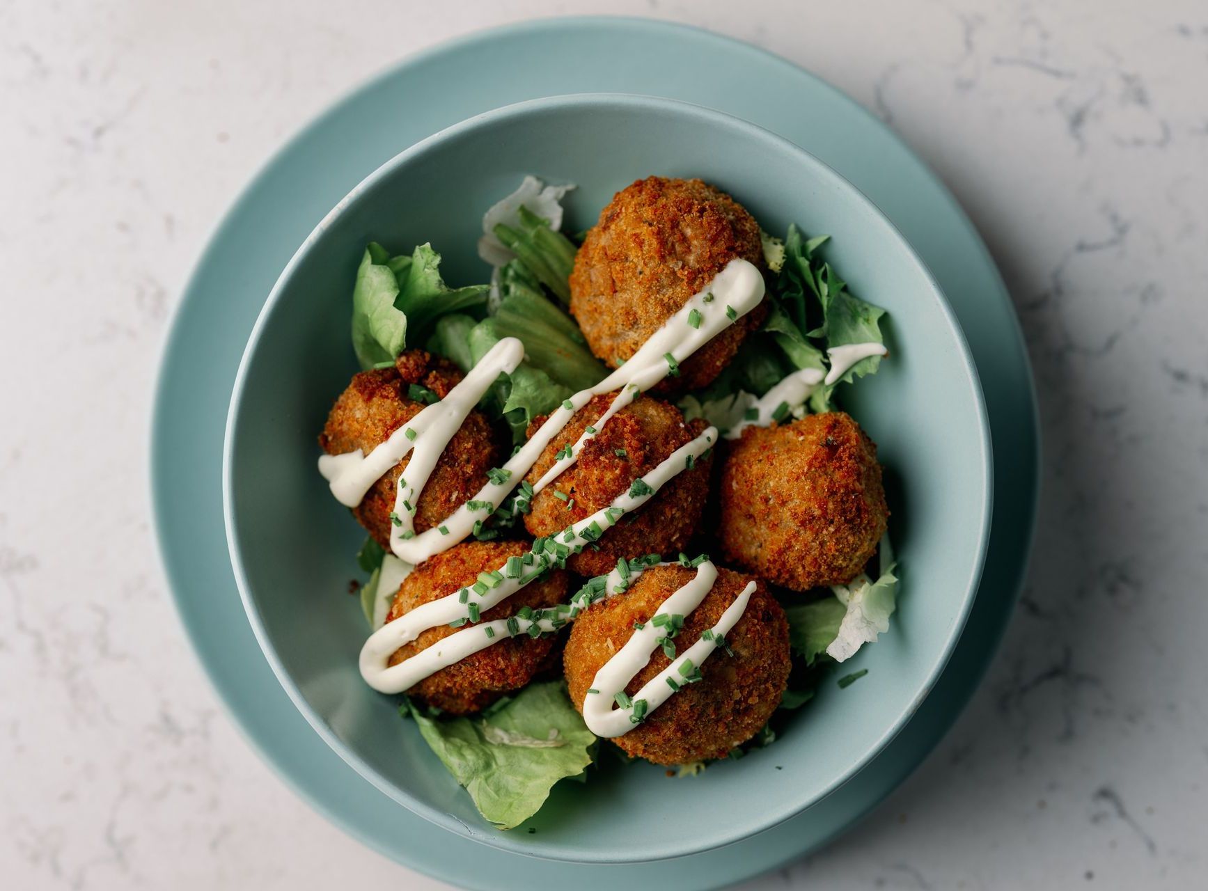 Plate of breaded falafel on lettuce, drizzled with white sauce, on a pale blue dish