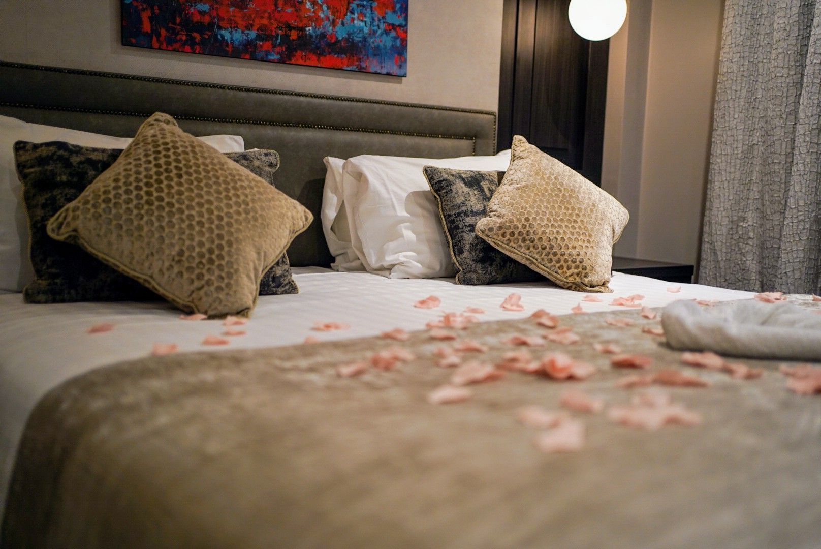 Romantic hotel bed with beige pillows, rose petals, and soft lighting