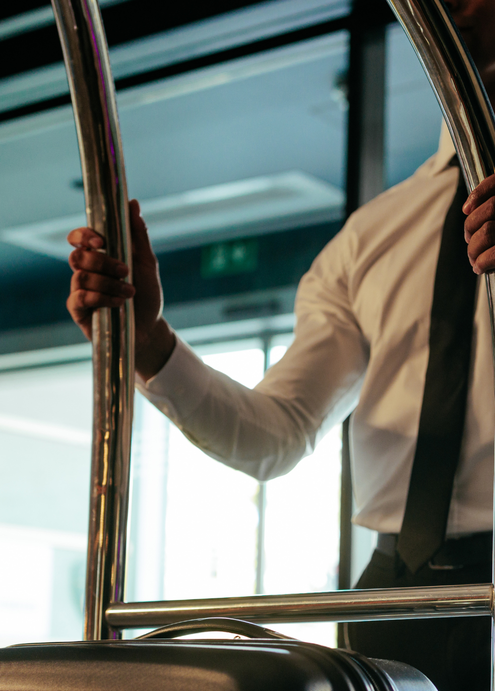 Person in a white shirt and black tie holding chrome rails inside a bus or train