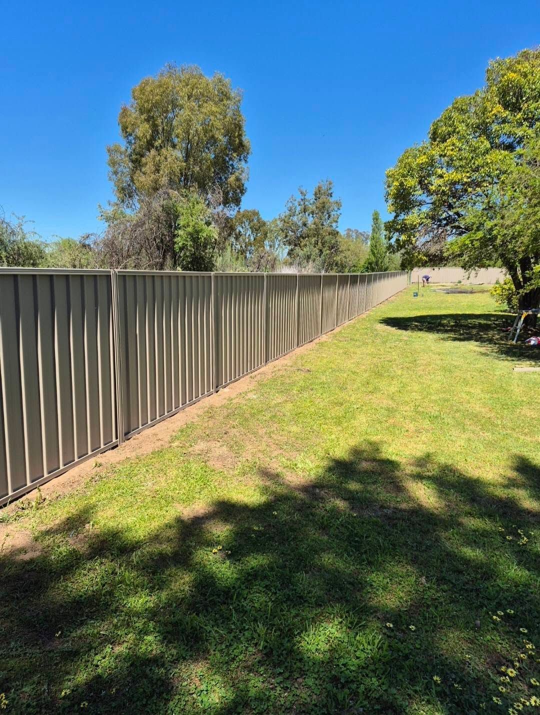 A Long, Beige Corrugated Fence in a Grassy Backyard — Precision Fencing & Landscaping in Thurgoona, NSW