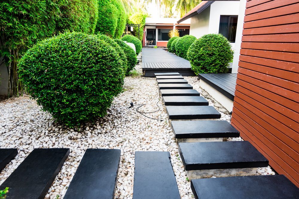 A Garden Path of Black Stepping Stones With Rounded Green Bushes — Precision Fencing & Landscaping in Thurgoona, NSW
