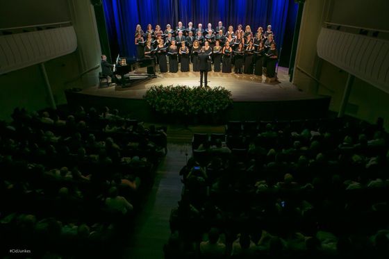 Vista do alto do Teatro Álvaro de Carvalho, com o coral no palco sob cortina azul e a plateia na penumbra