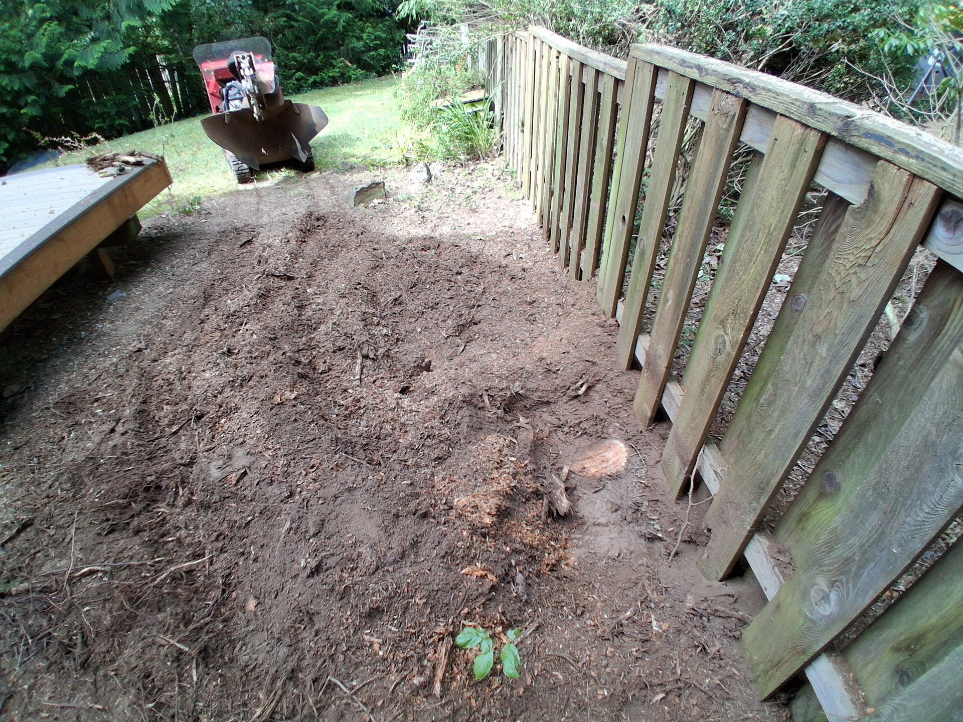 Mud-covered path beside a wooden fence, with a wheelbarrow at the far end and a bench on the left.