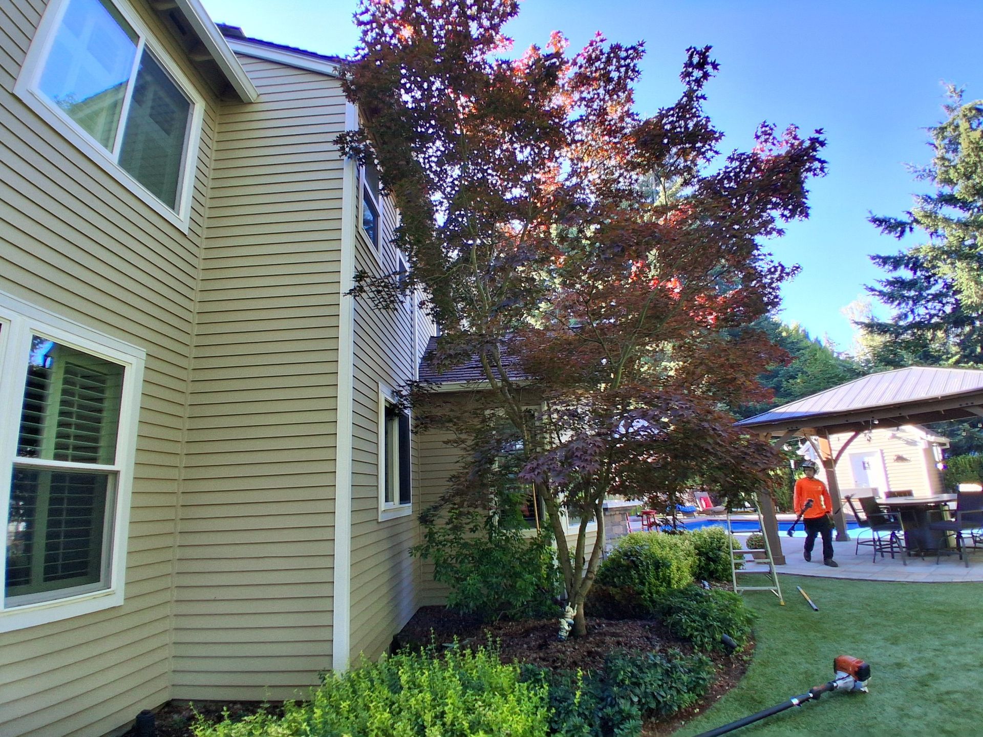 Suburban house exterior with trees, shrubs, and a person in an orange shirt in the background