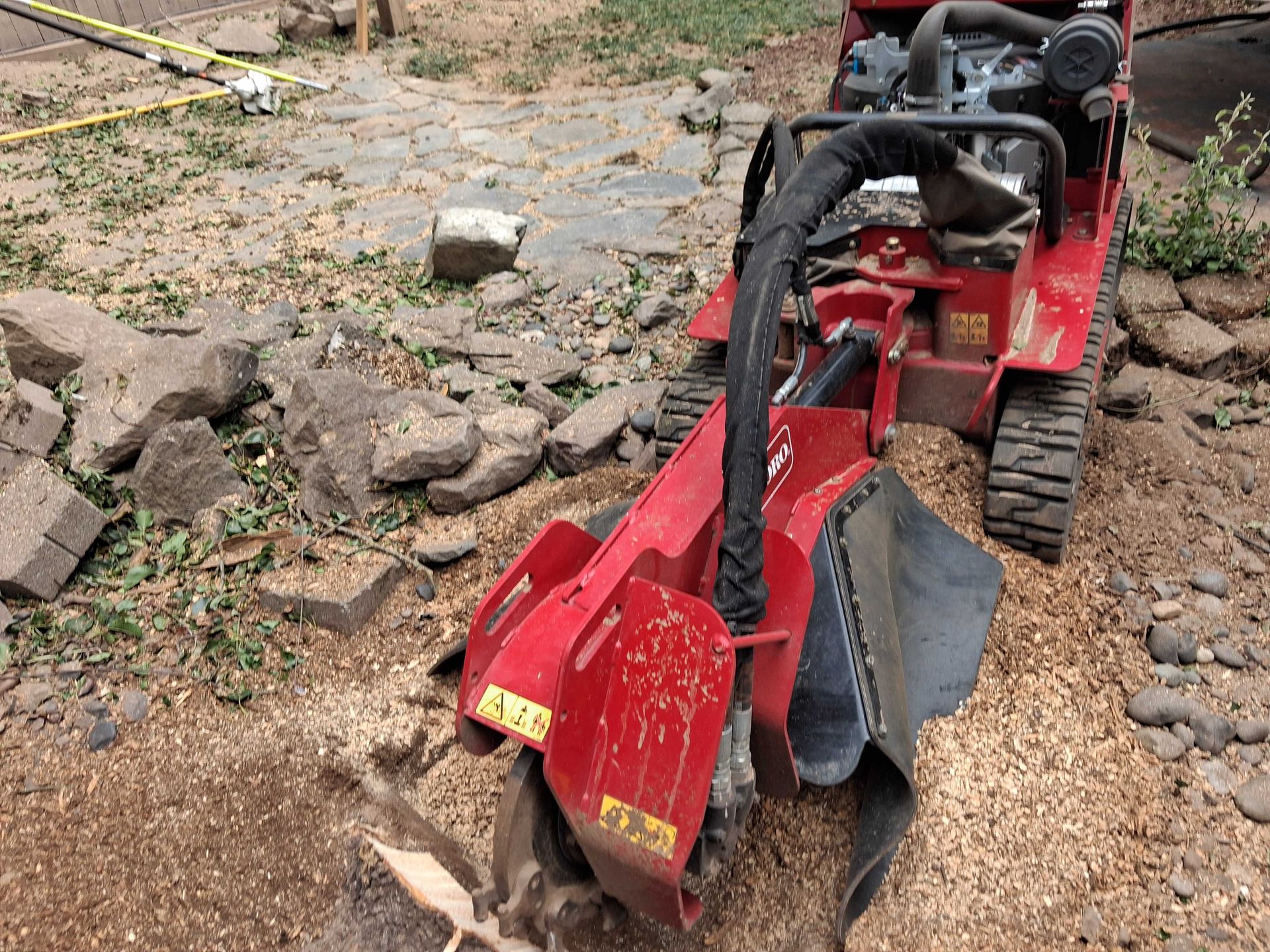 Red tracked mini excavator with auger attachment on rocky dirt ground outdoors