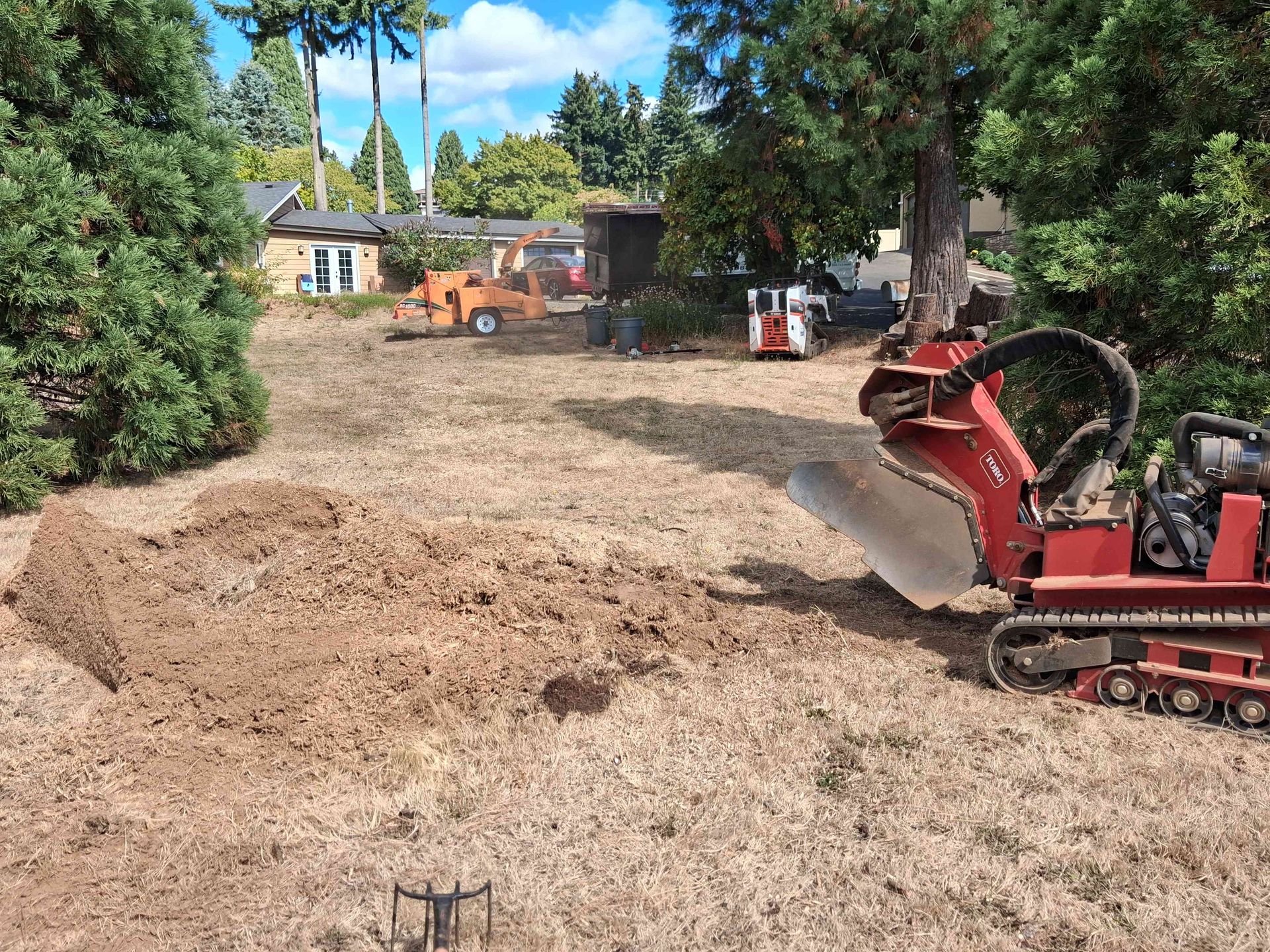 Backyard excavation with piles of dirt and a red mini excavator near trees and a house