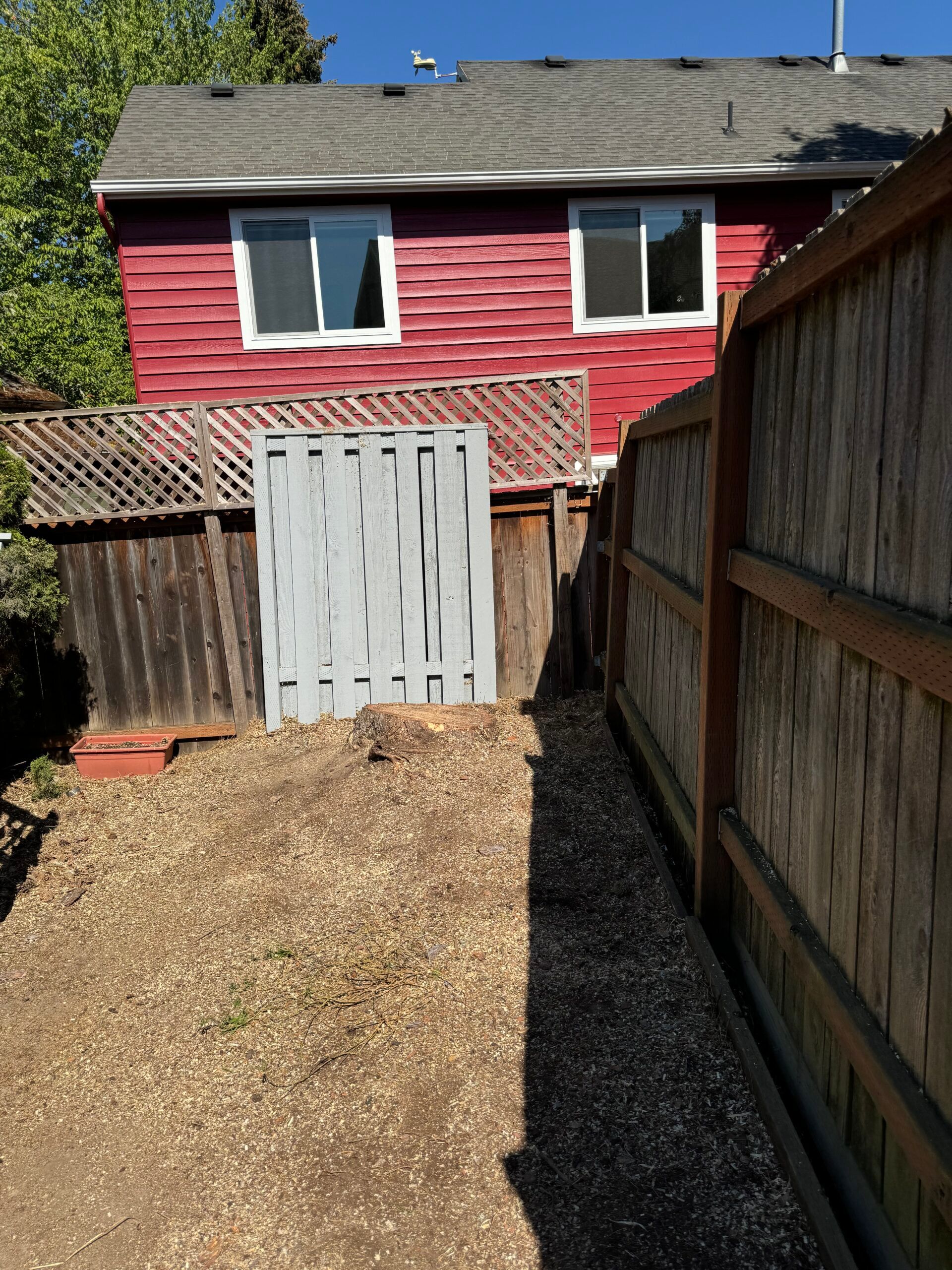 Narrow gravel path leading to a red house with white doors and windows beside wooden fences