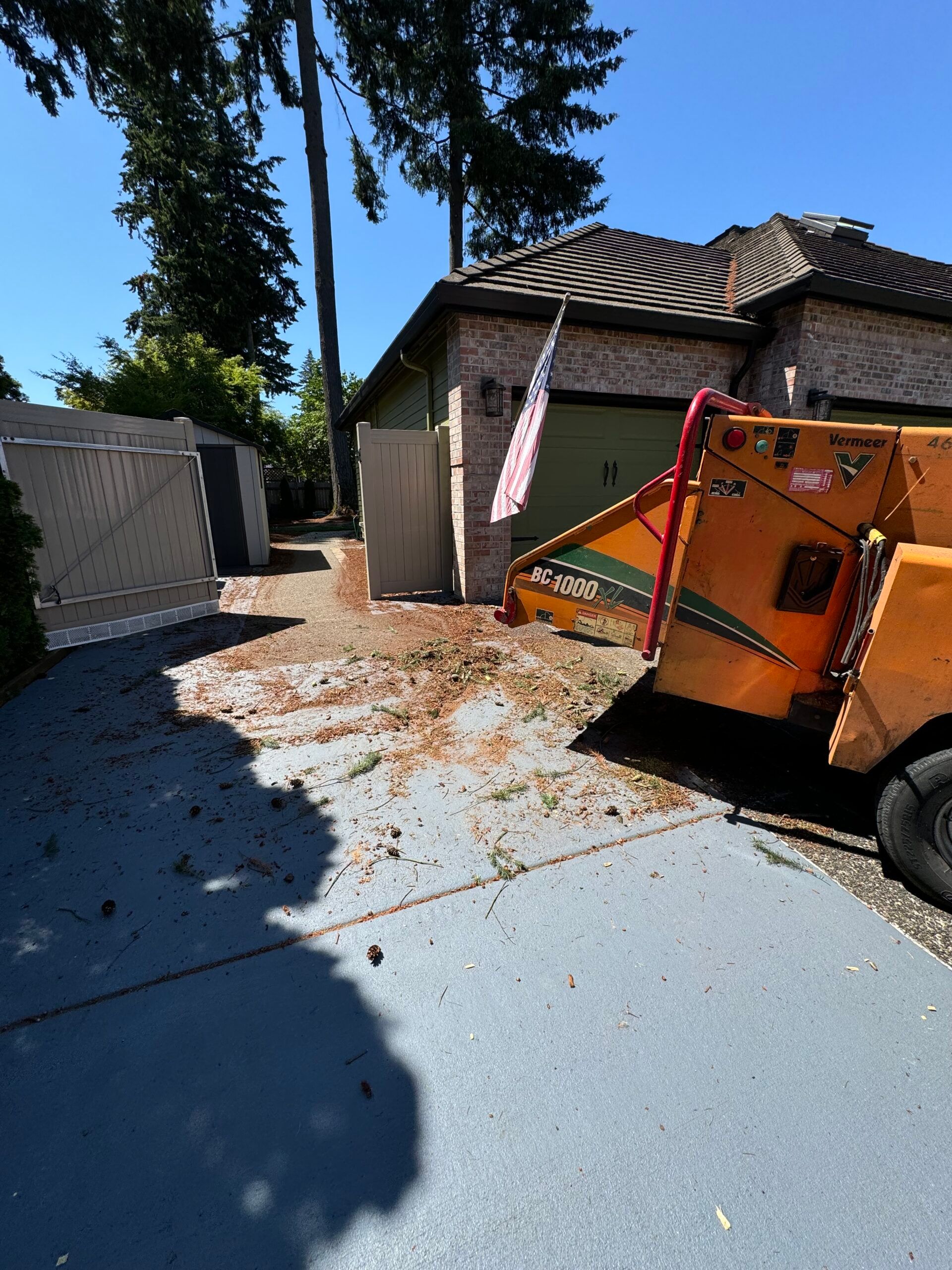 Orange trailer on a blue driveway with debris, beside a house and trees on a sunny day