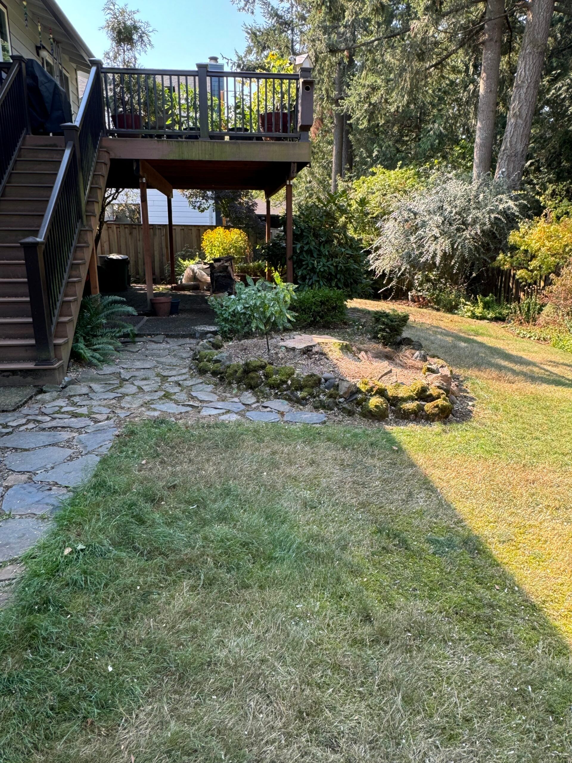 Backyard with wooden deck, stone patio, lawn, and garden beds in bright sunlight