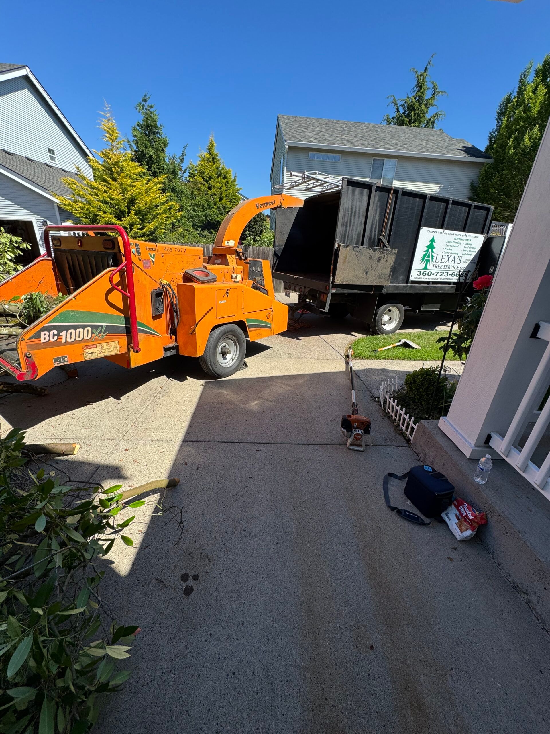 Orange wood chipper unloading a black trailer in a sunny driveway