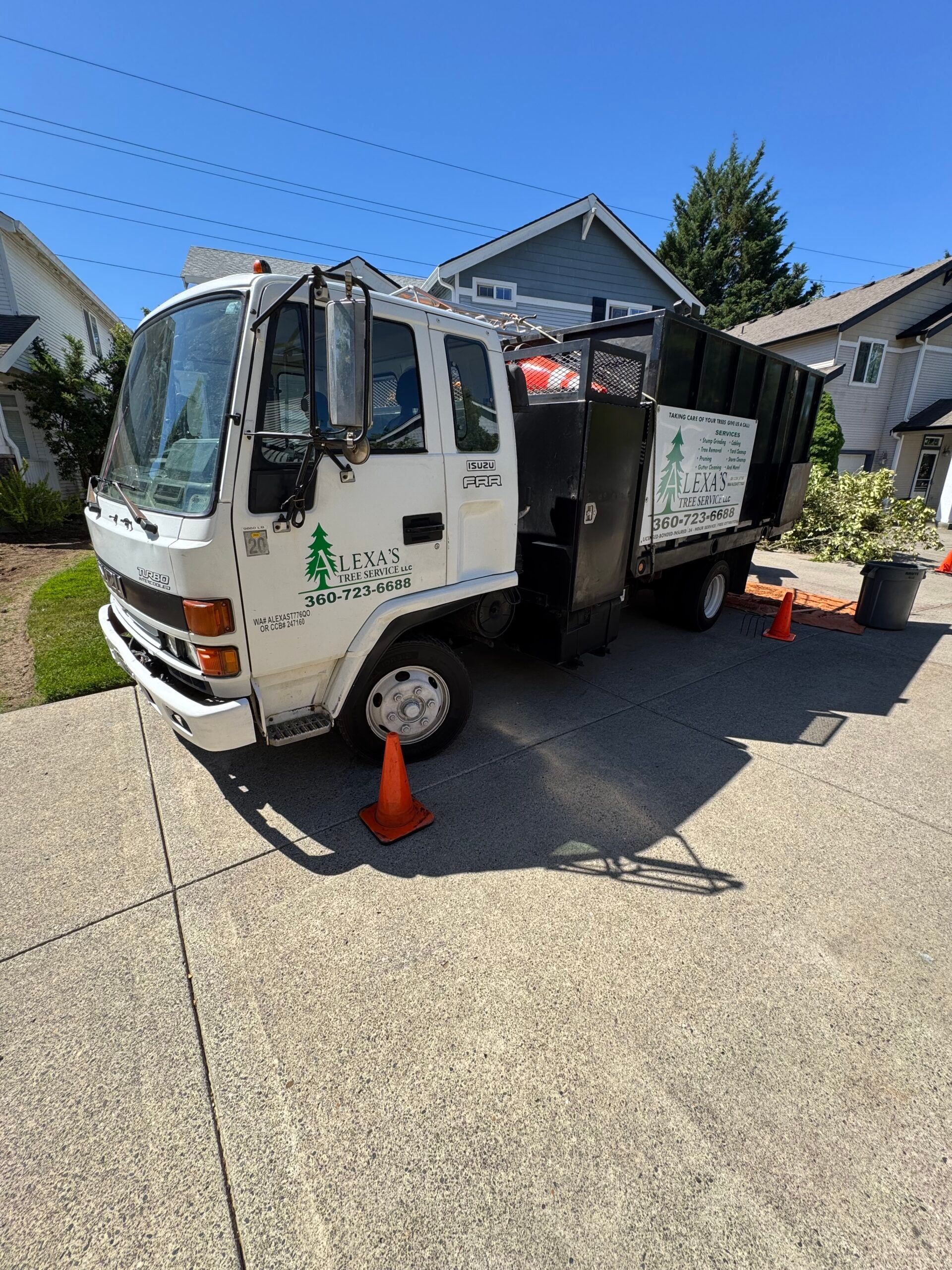 White utility truck parked on a driveway with orange cones and equipment in the back, residential street setting