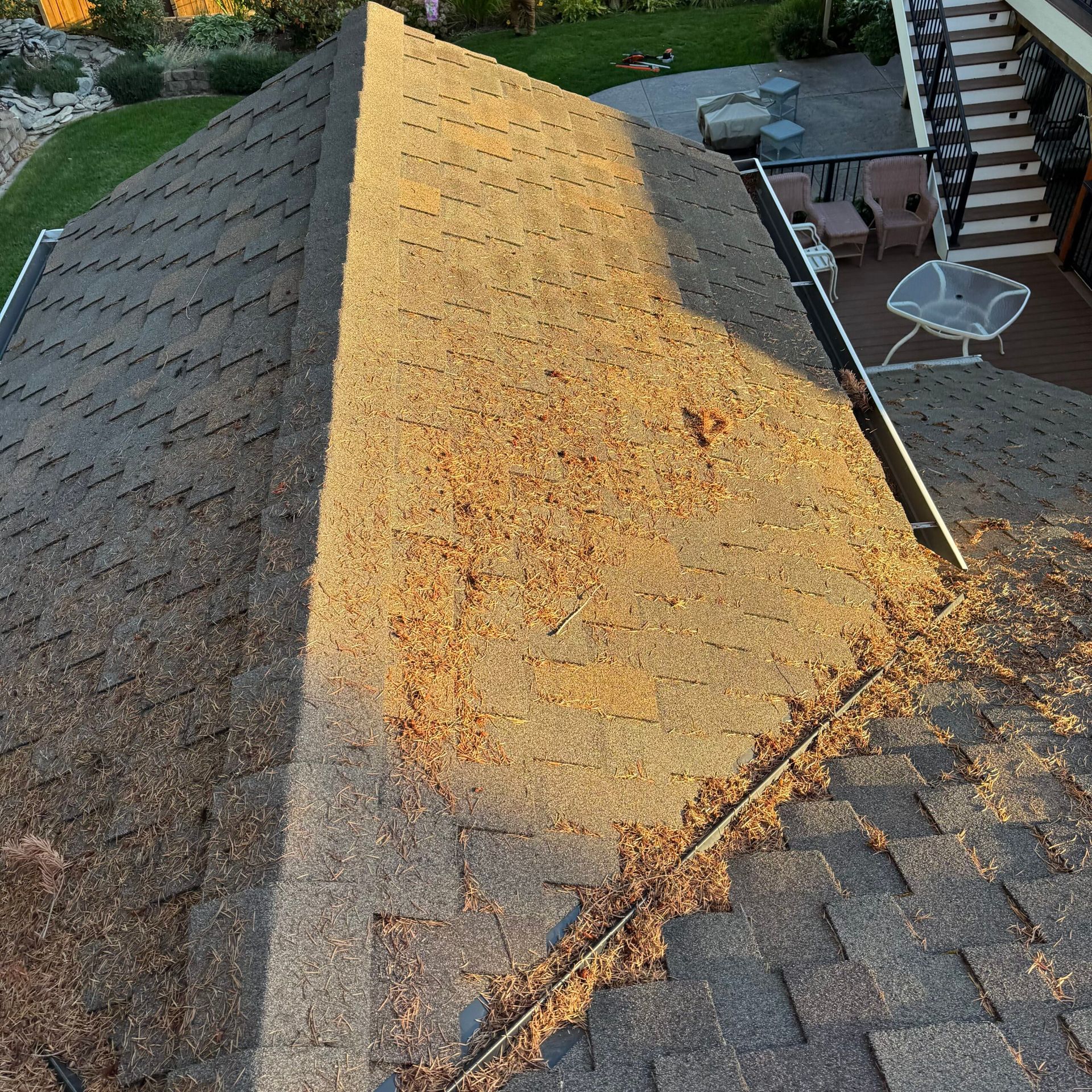 Rooftop with a large yellow-brown shingled ridge beside dark gray shingles and a patio below.