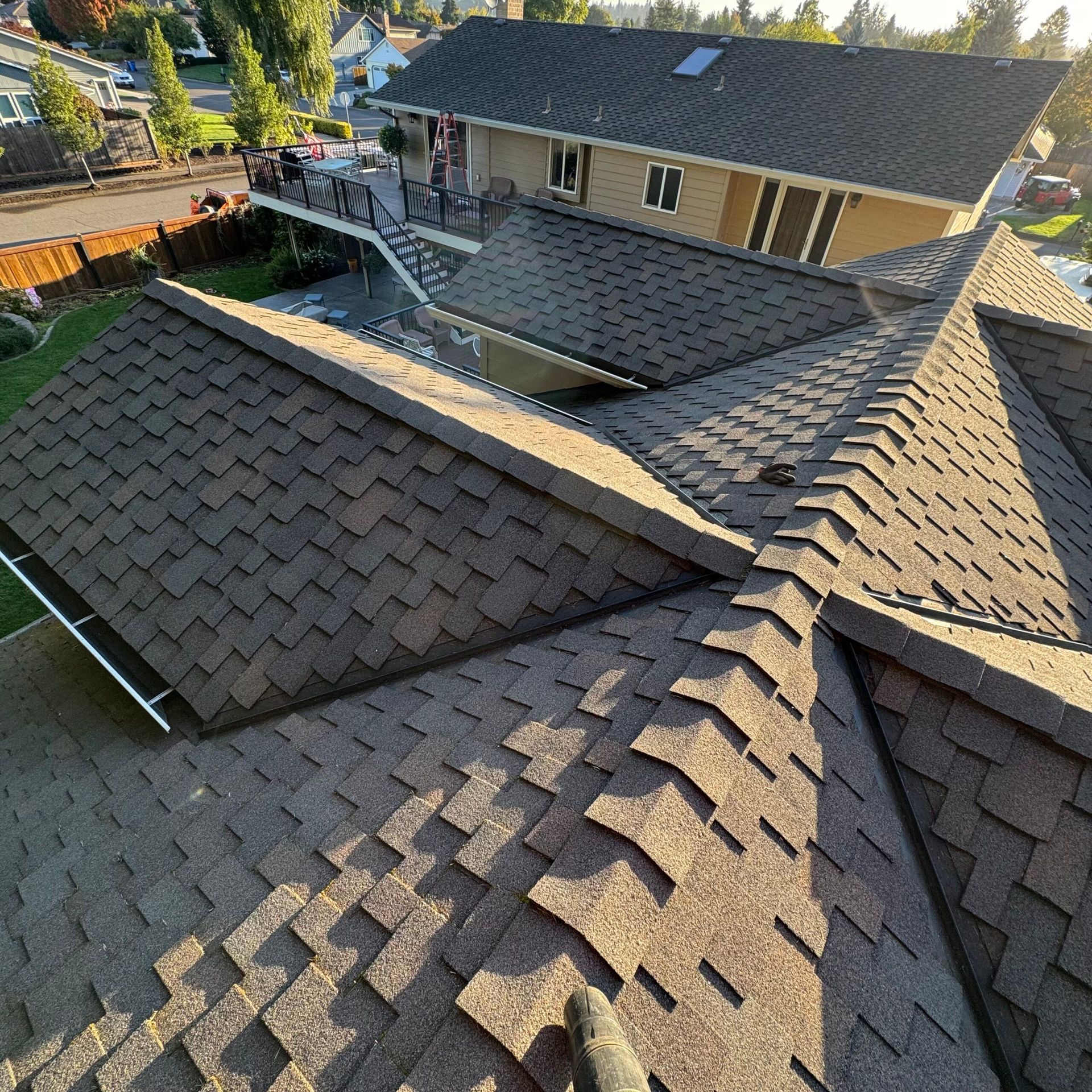 Roofing work on a house with dark gray shingles, viewed from above in a residential neighborhood