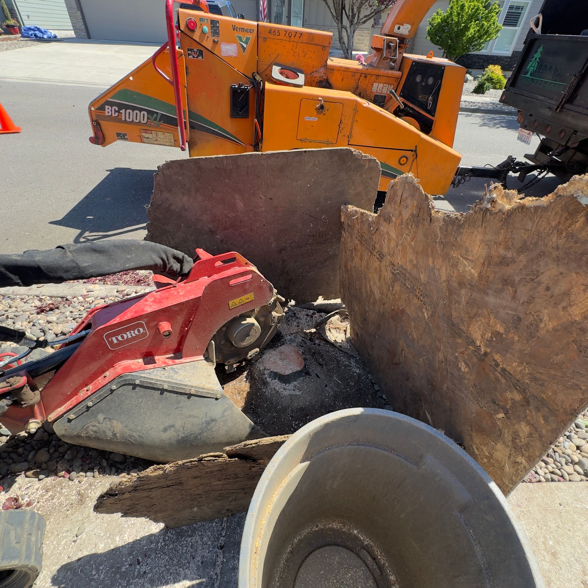 Construction site with orange machinery, red skid steer, and large rusted metal sheet debris on pavement