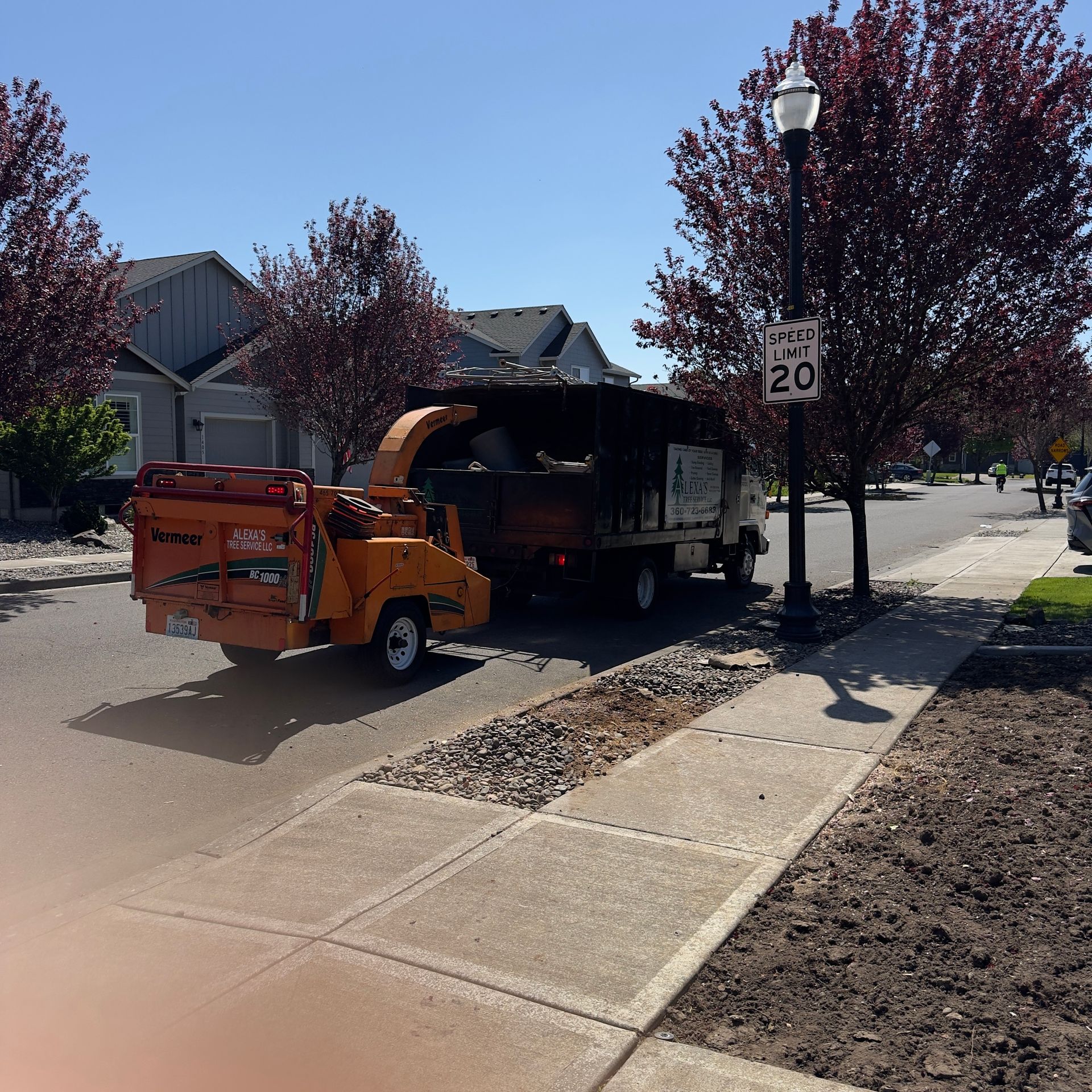 Orange utility truck parked on a sidewalk beside a residential street, with a speed limit sign nearby.