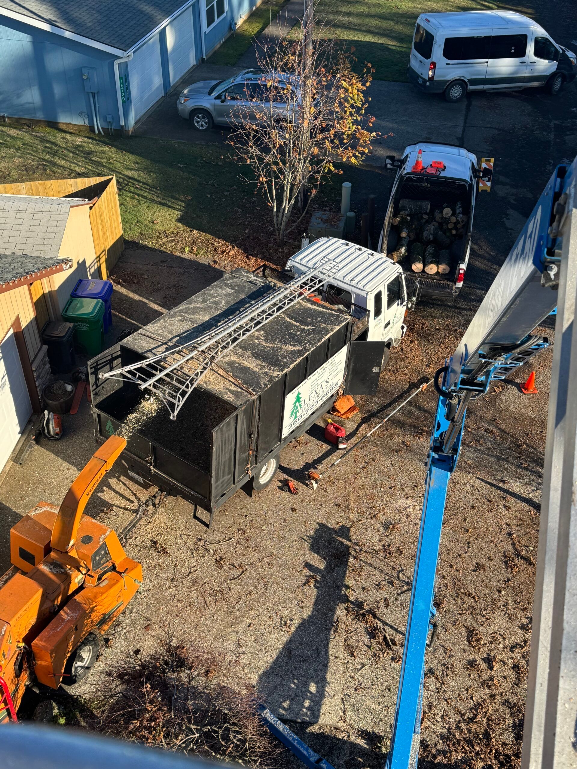 Backyard construction site with a dumpster, excavator, and white utility truck near a house