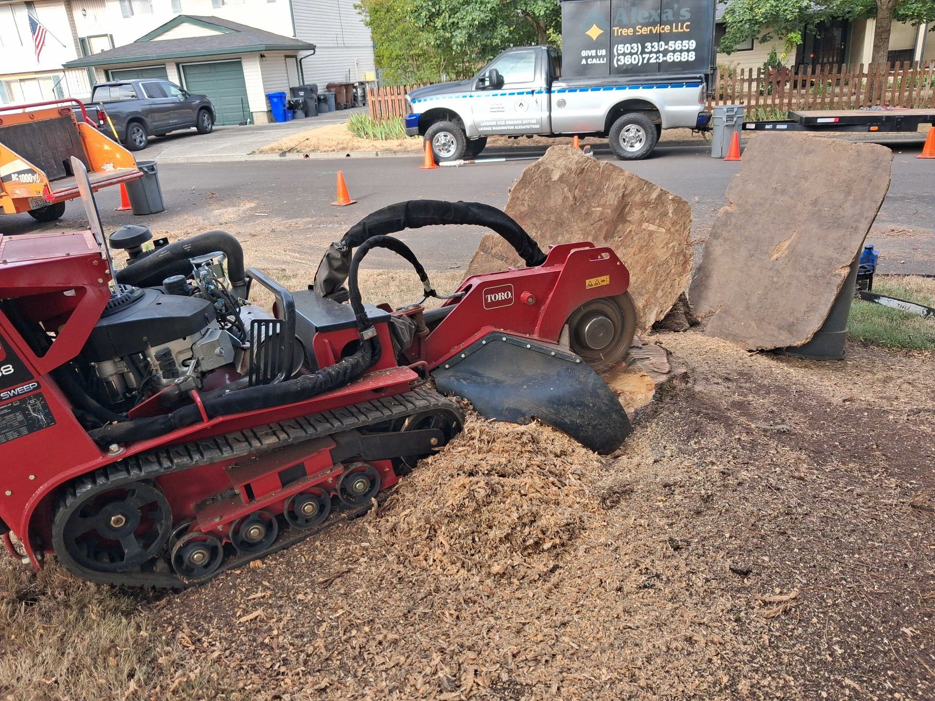 Red track loader pushing wood chips near large boulders at a worksite with a pickup truck nearby