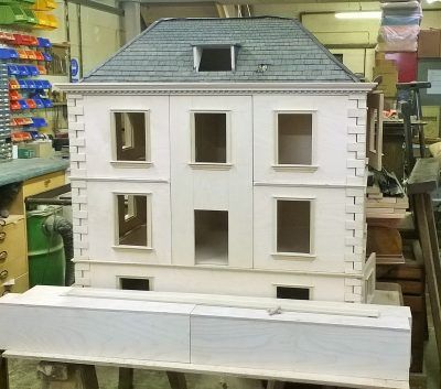 A white doll house with a blue roof is sitting on a table