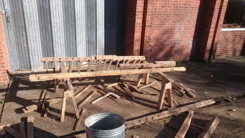 A bunch of wooden pieces are sitting on the ground in front of a brick building.