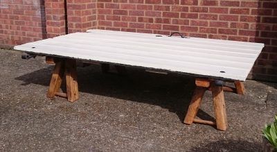 A large piece of wood is sitting on wooden legs in front of a brick wall.
