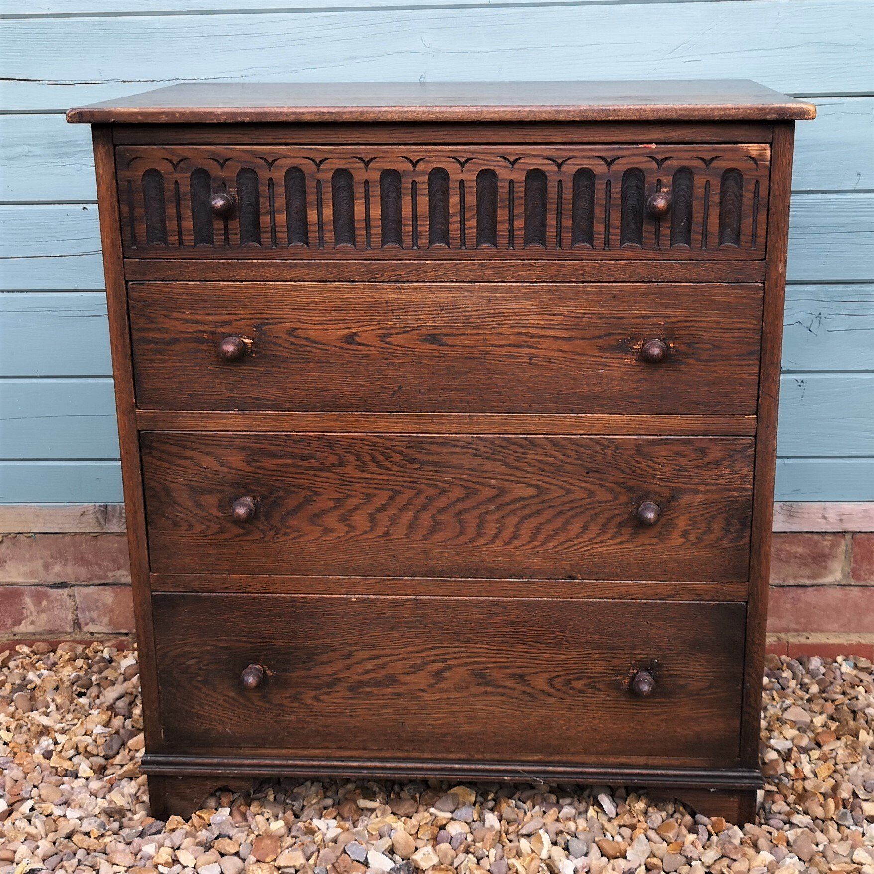 A wooden chest of drawers is sitting on a pile of gravel in front of a blue wall.