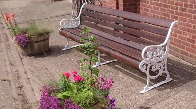 A wooden bench is sitting in front of a brick building next to a potted plant.