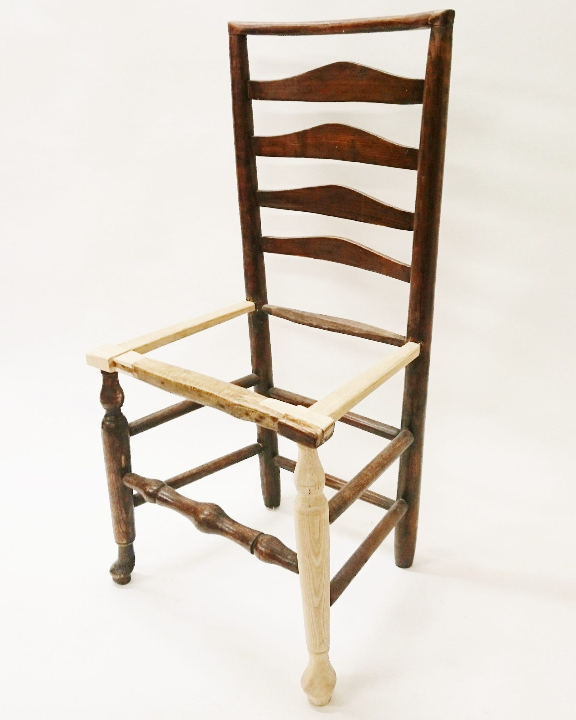 A wooden chair without a seat is sitting on a white surface