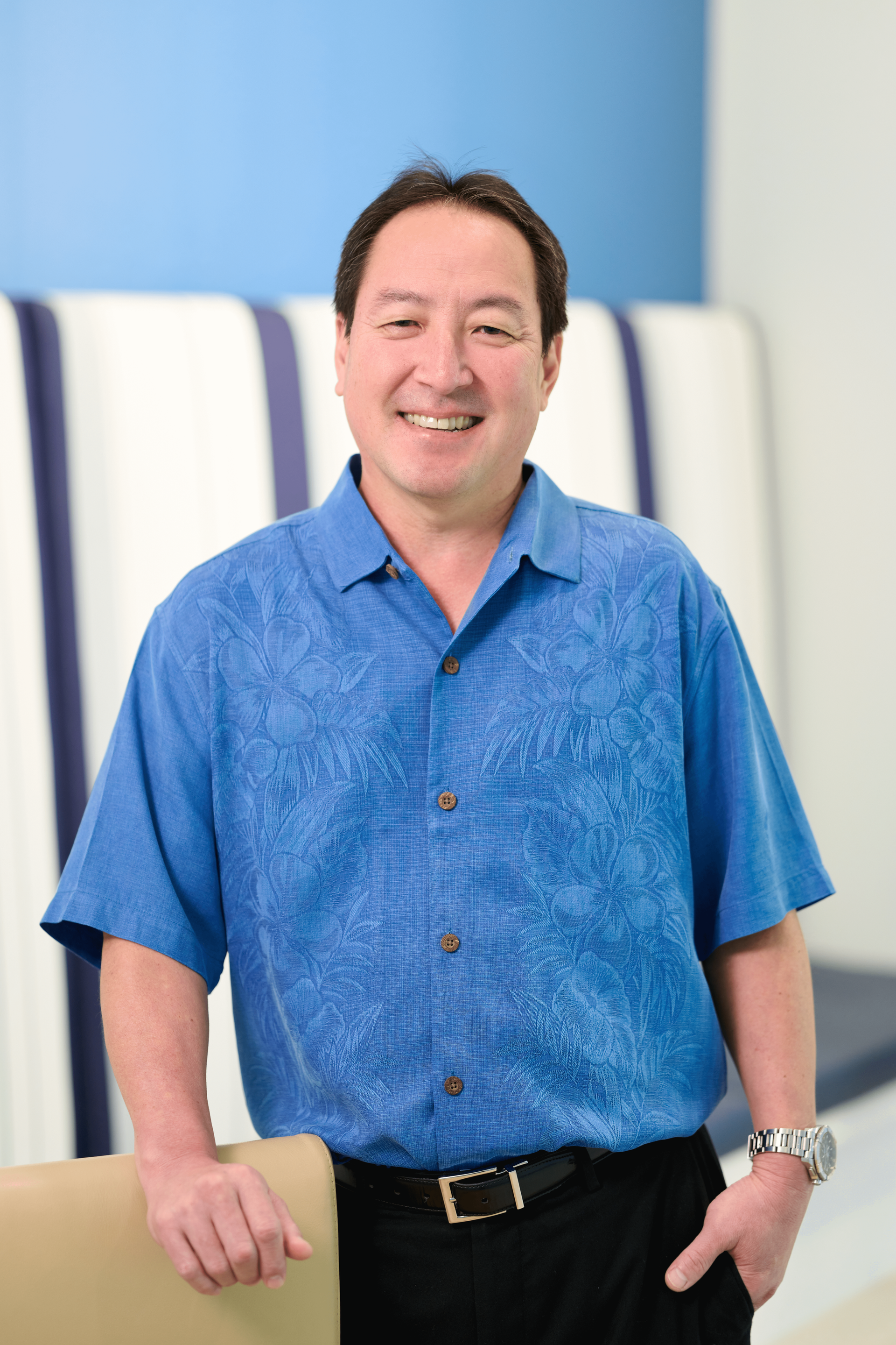 Chad Funasaki, Audit Principal, standing and wearing a blue aloha print shirt at the N&K CPA accounting firm office in Downtown Honolulu