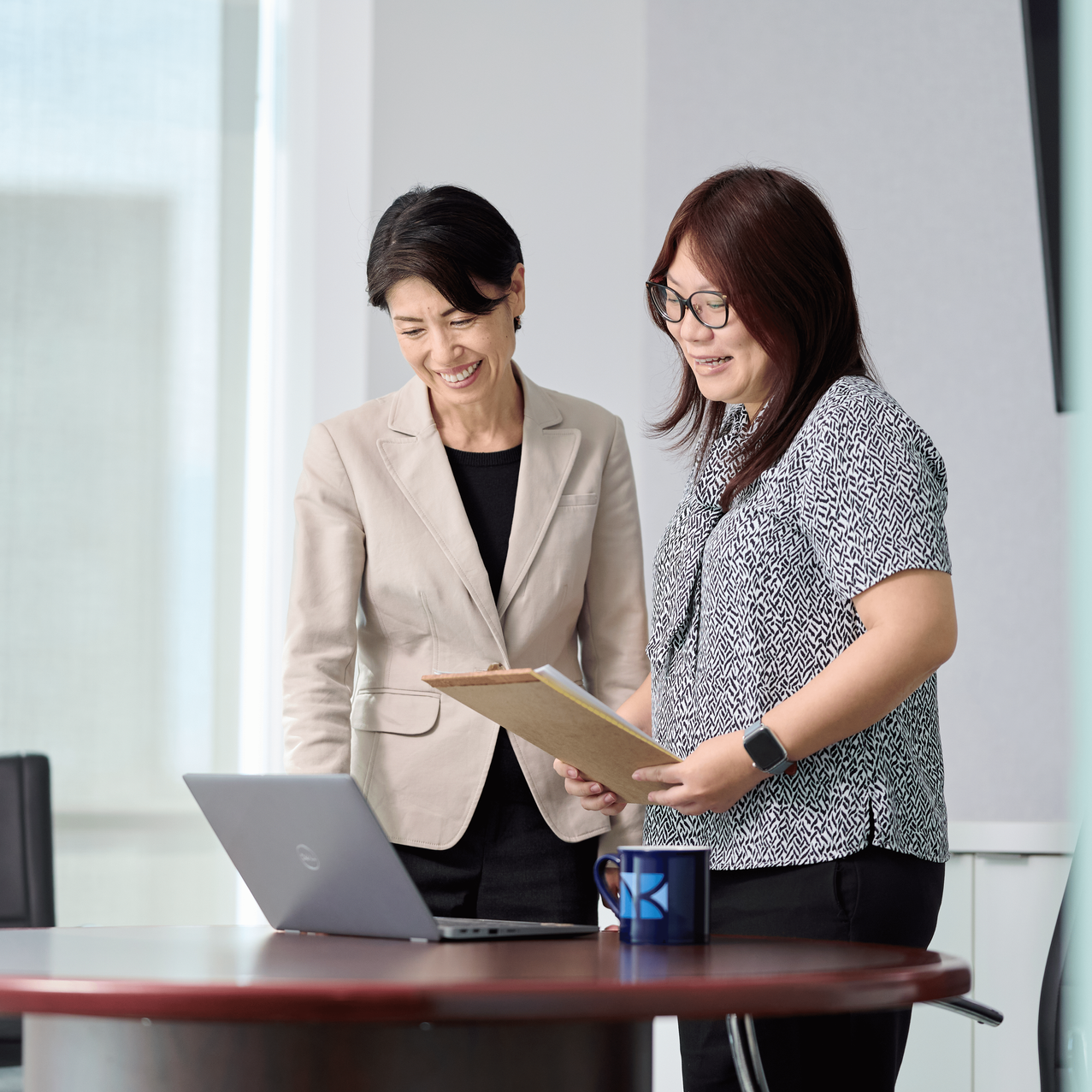 two women discussing client advisory services oahu, one holding a manila folder with information on accounting and compliance.