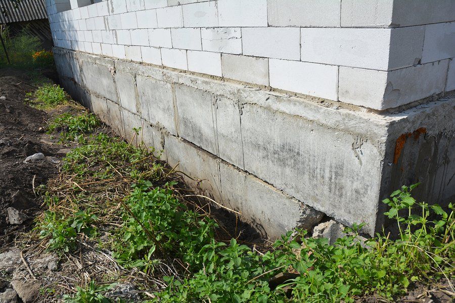 A brick wall with a concrete base is surrounded by grass and dirt.