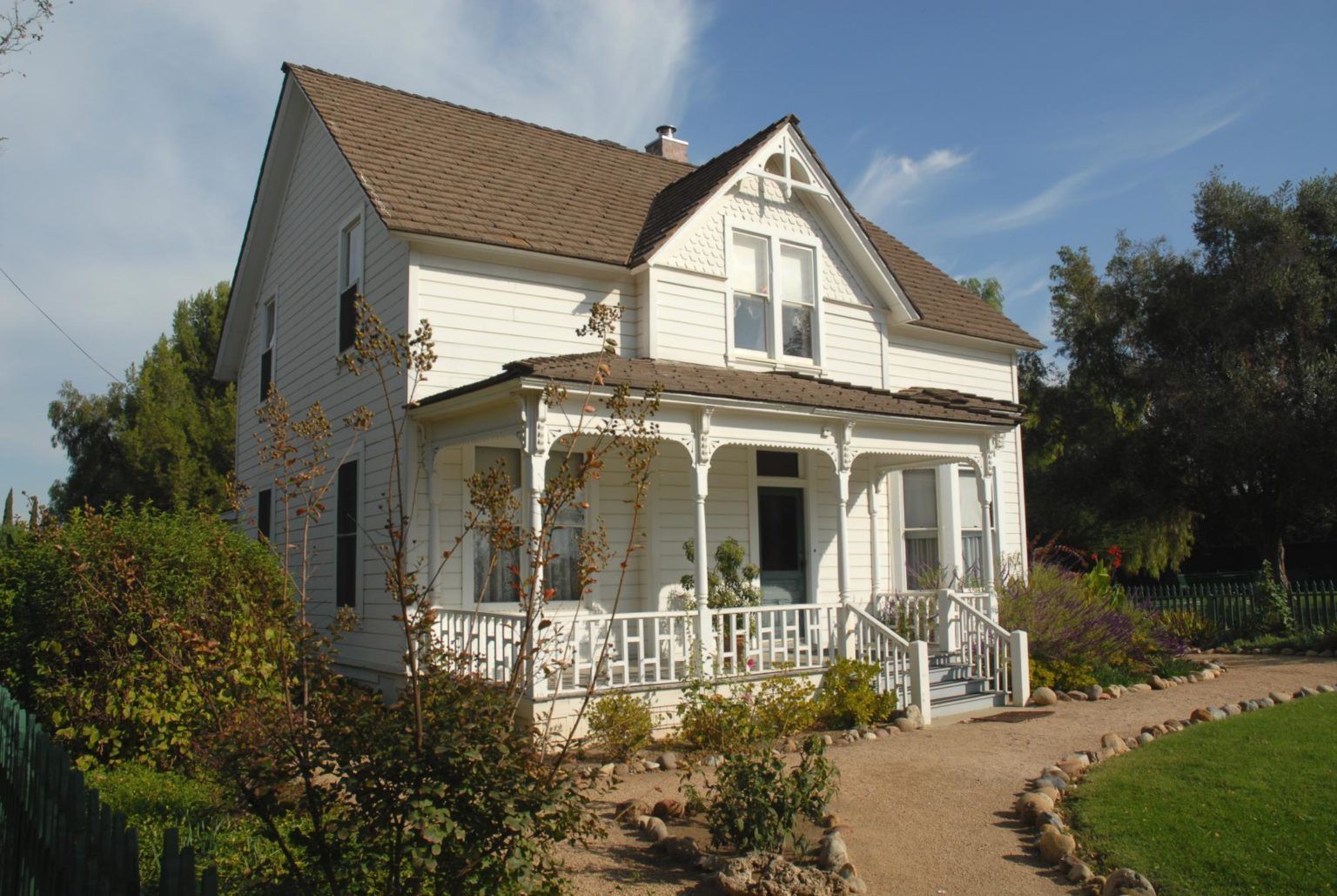 A white house with a brown roof and a large porch
