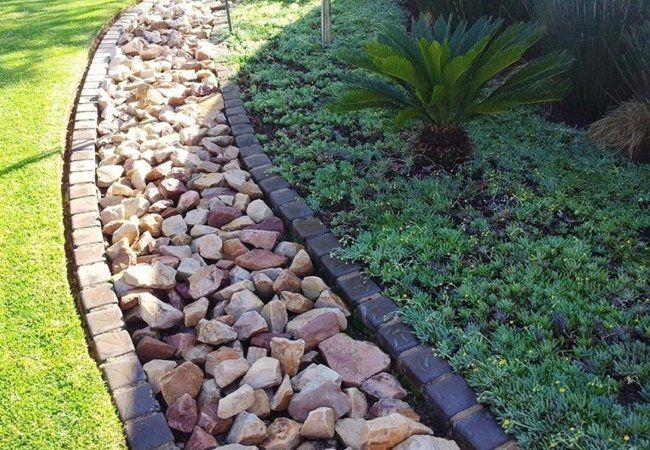 A stone walkway in a garden with a brick border