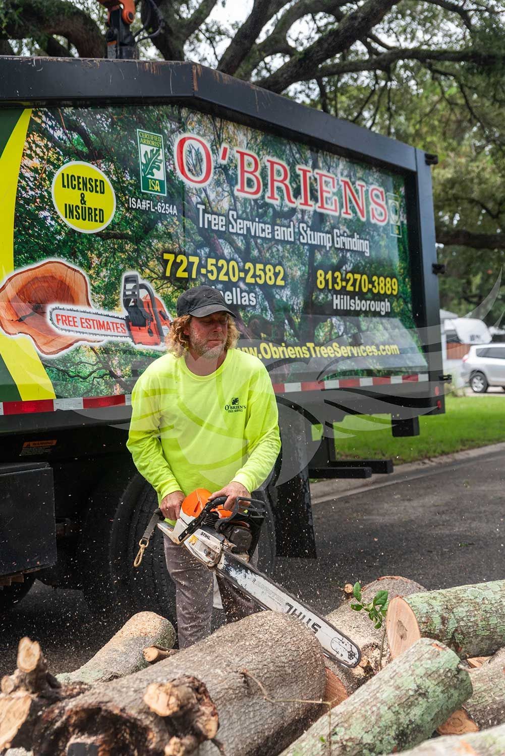 A man is cutting a log with a chainsaw in front of a truck.