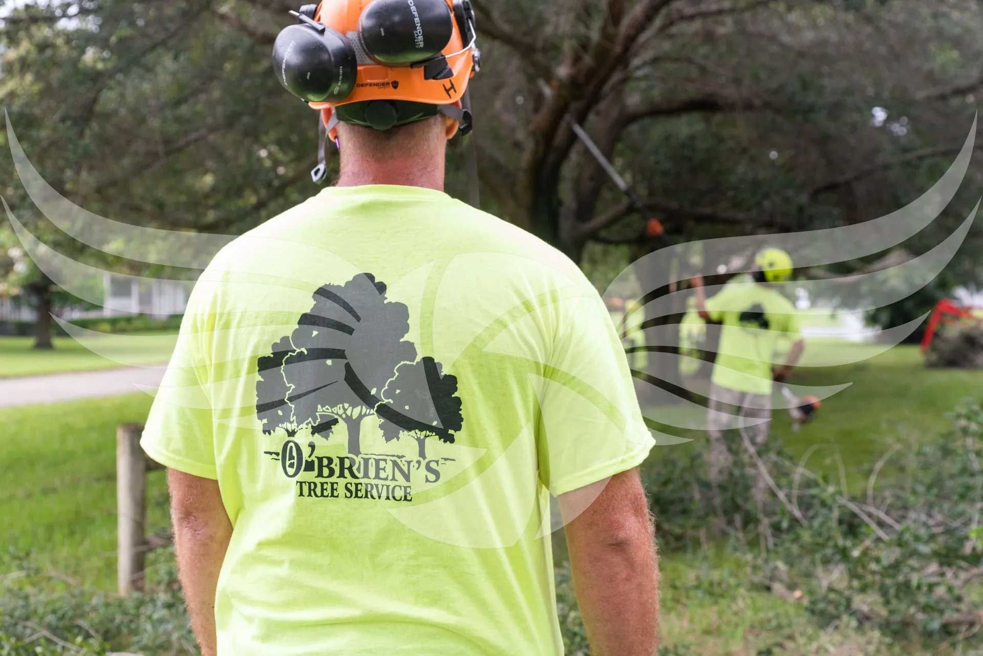 A man wearing a helmet and a neon yellow shirt is standing in front of a tree.