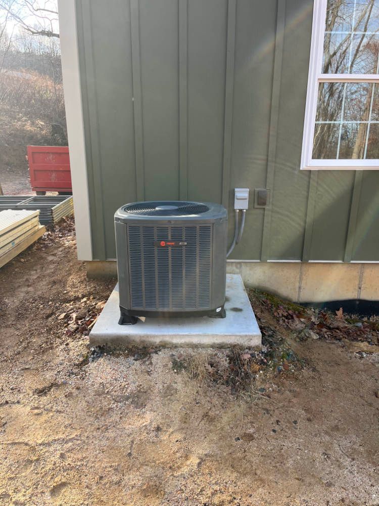 An air conditioner is sitting on a concrete platform in front of a house.