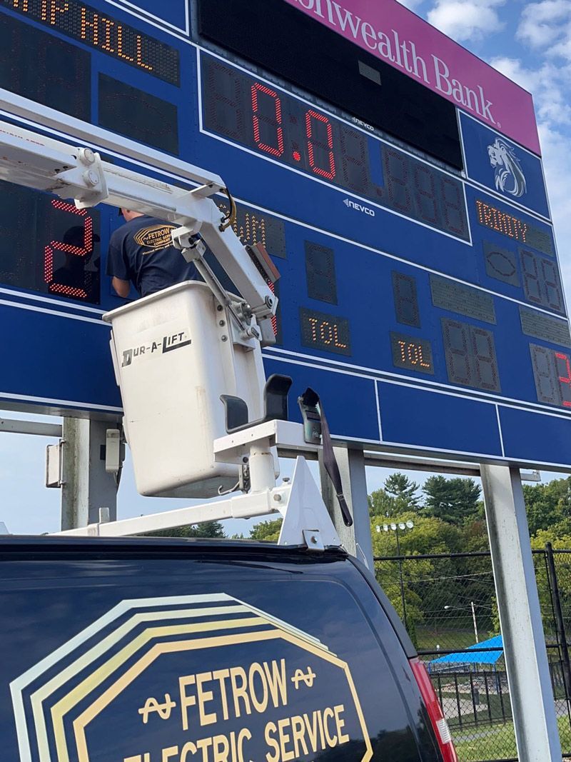 A man is working on a scoreboard next to a van that says fetrow electric service