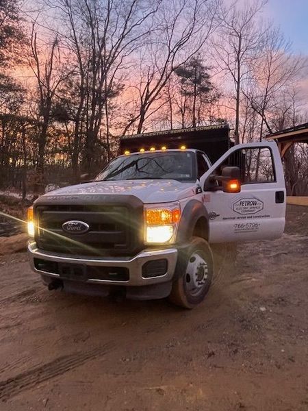 A white ford truck is parked on a dirt road with its doors open.