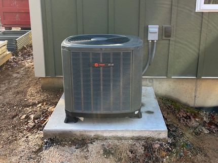 A gray air conditioner is sitting on a concrete platform in front of a green building.