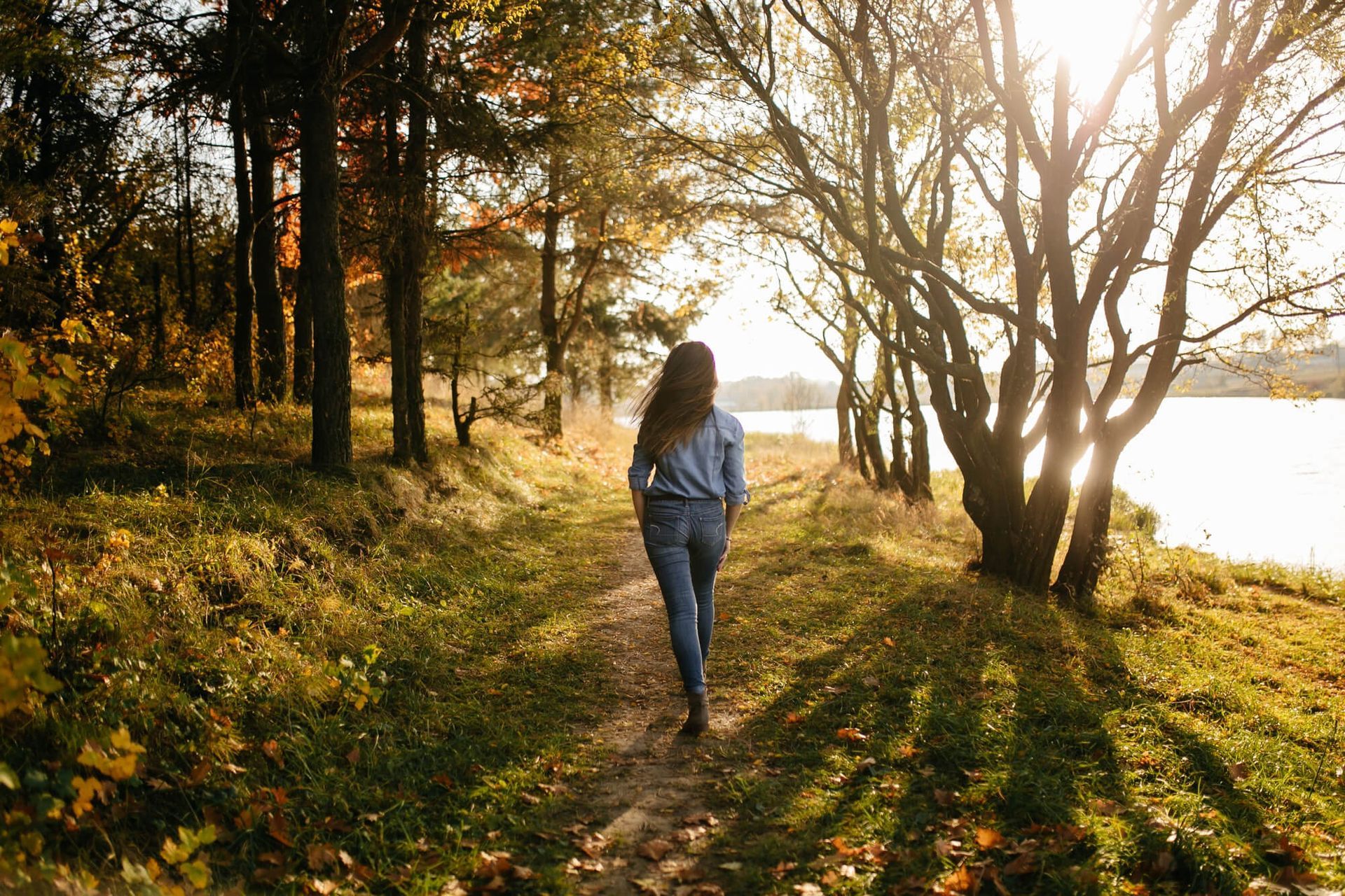 Una mujer camina por un sendero en el bosque cerca de un lago.