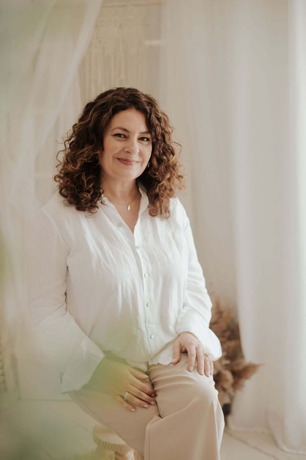 Mónica García Hidalgo con una camisa blanca está sentada en una silla frente a una ventana.