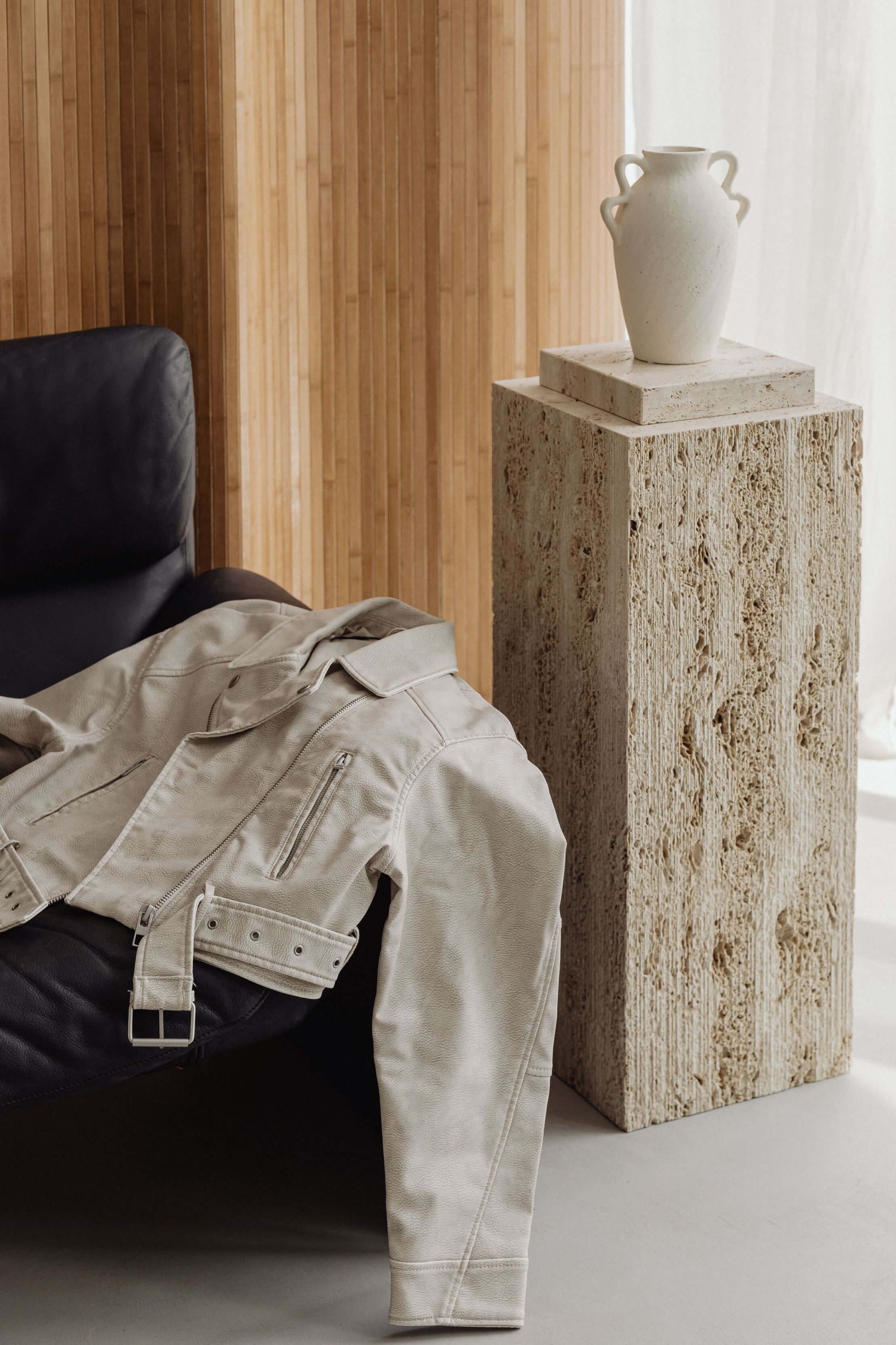 Una chaqueta está colocada sobre una silla al lado de un jarrón sobre un pedestal.