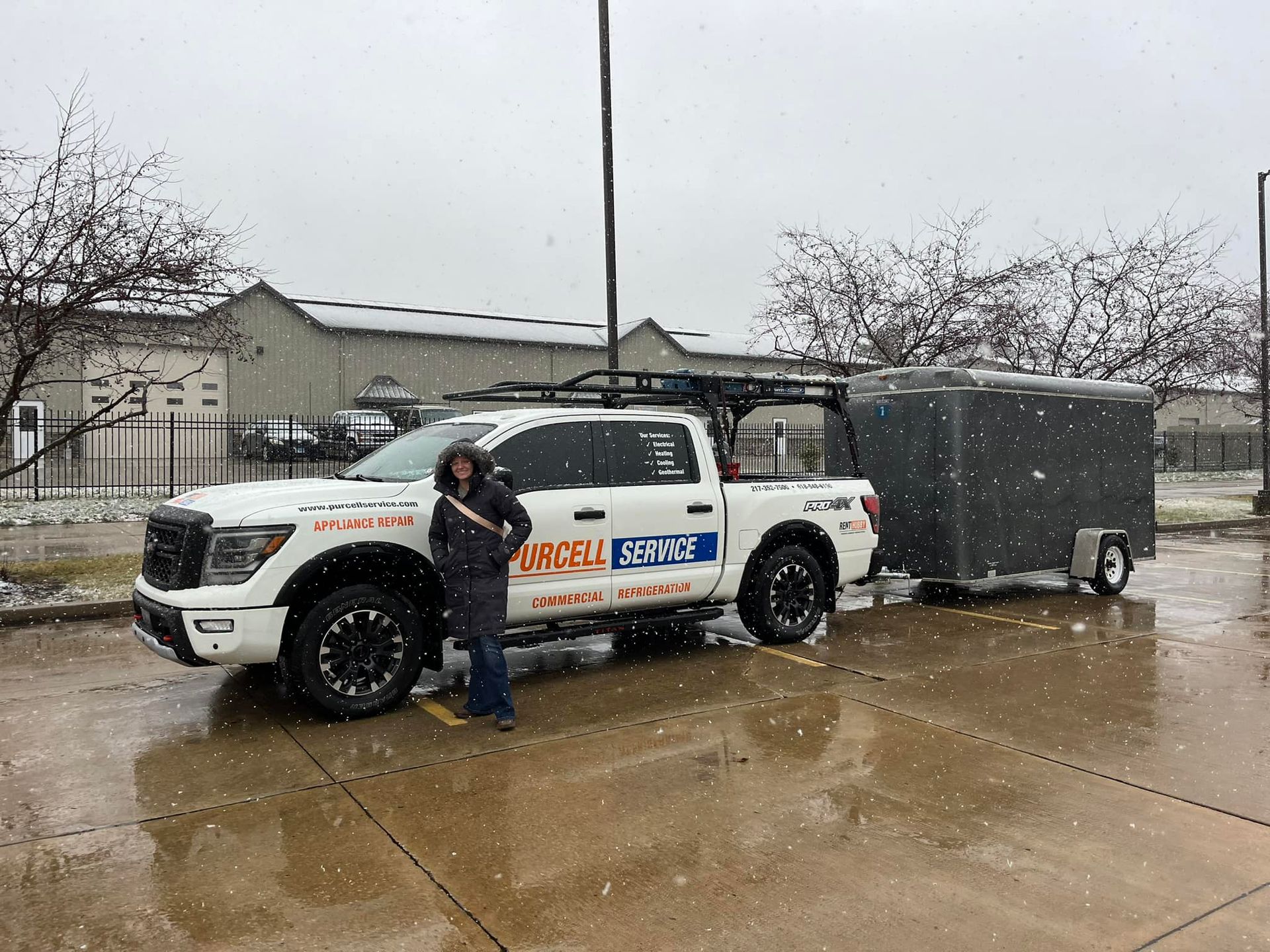 A man is standing next to a white truck with a trailer attached to it.