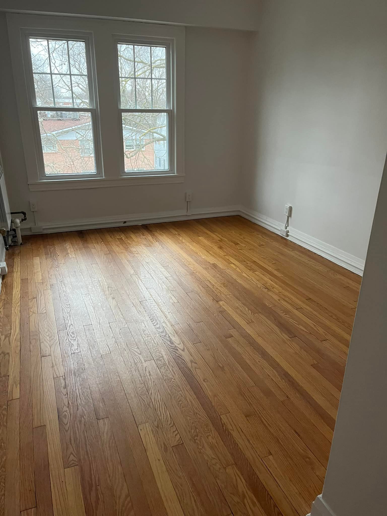 An empty room with hardwood floors and two windows.