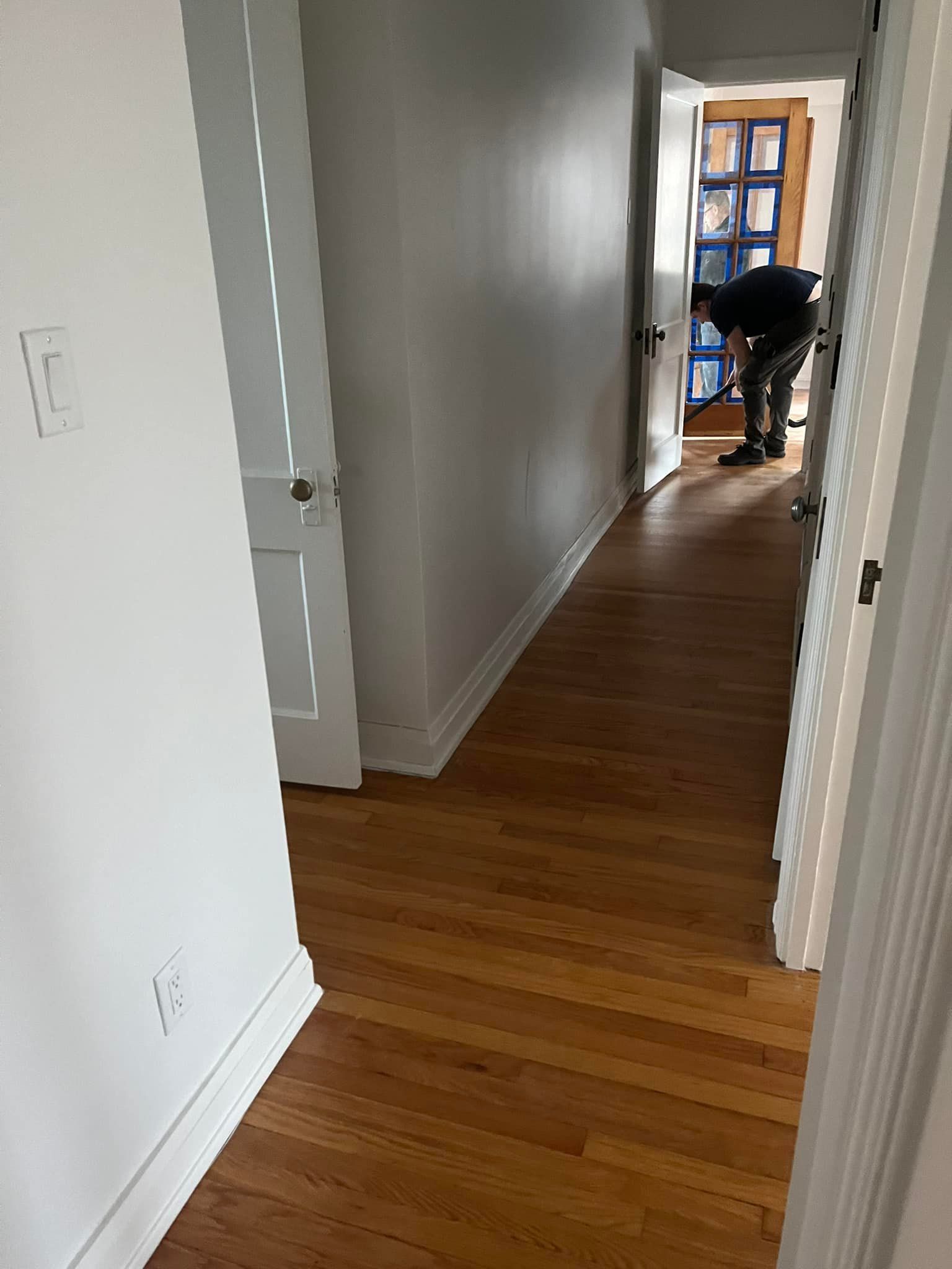 A man is standing in a hallway with hardwood floors and white walls.