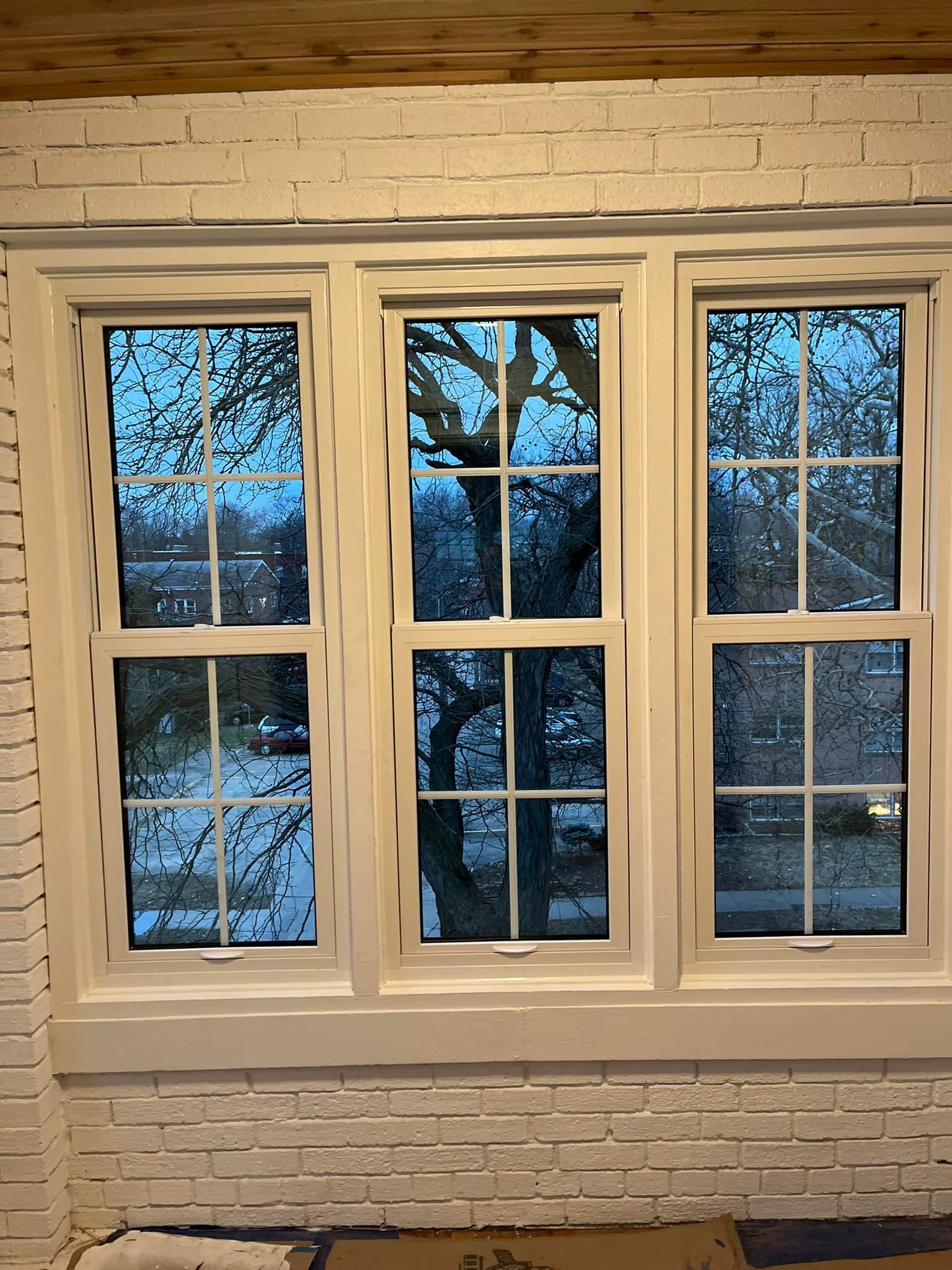 There are three windows in a room with a brick wall.